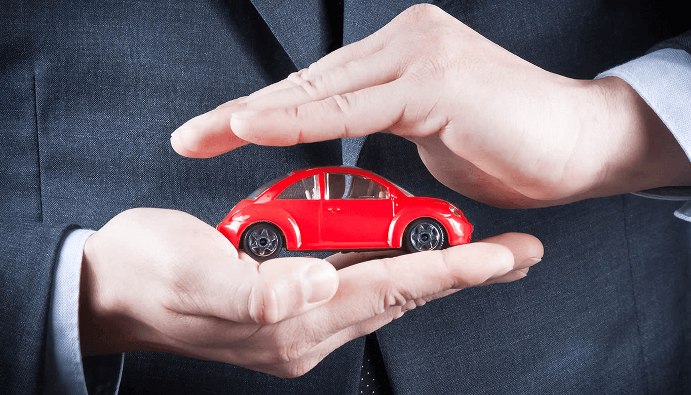 Manos protegiendo un vehículo en miniatura, representando seguros
